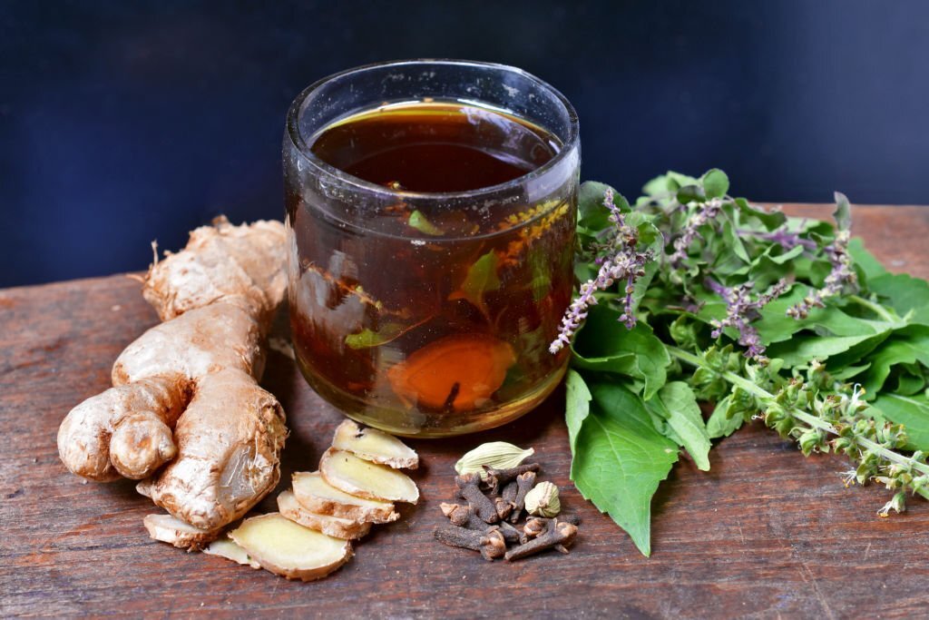 Ingredients in a small glass of Herbal Tea Ingredients are ginger, basil, cardamom, cloves on wooden table with black background